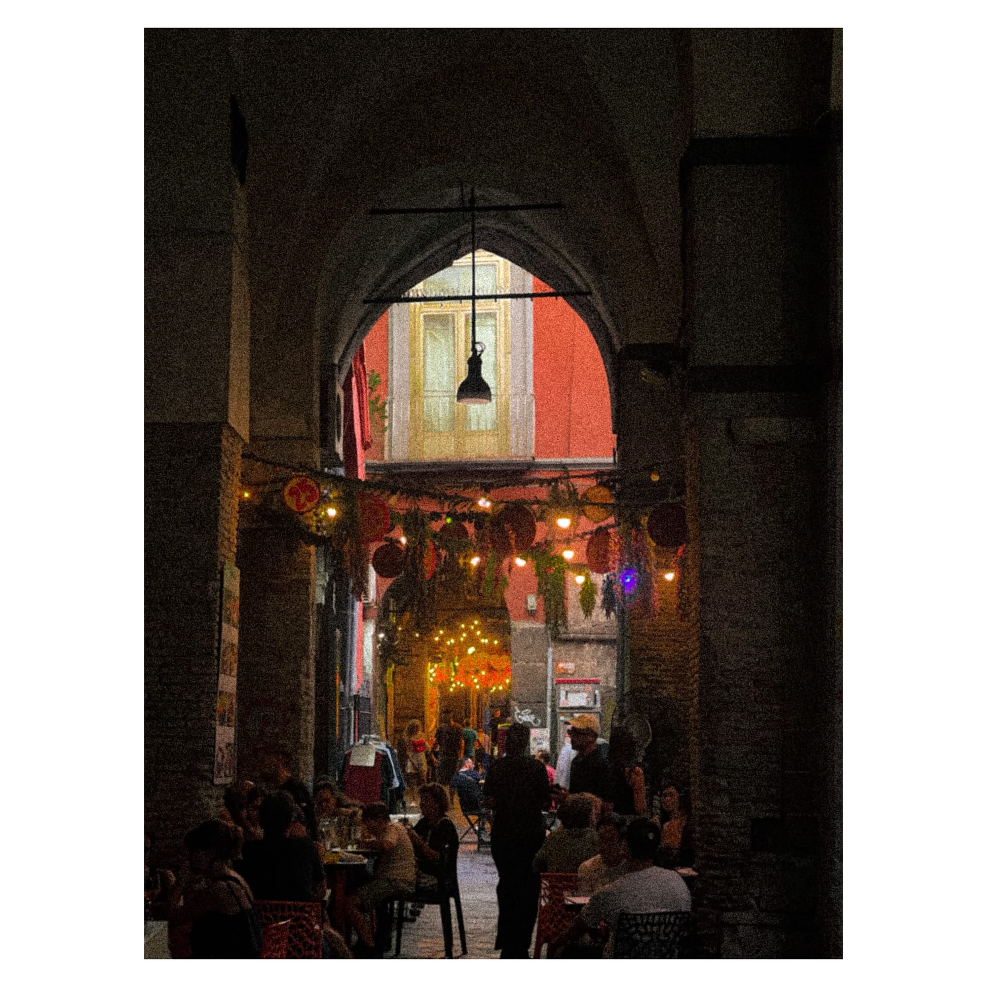 Lanterns strung down a vaulted alley with people dining outdoors.