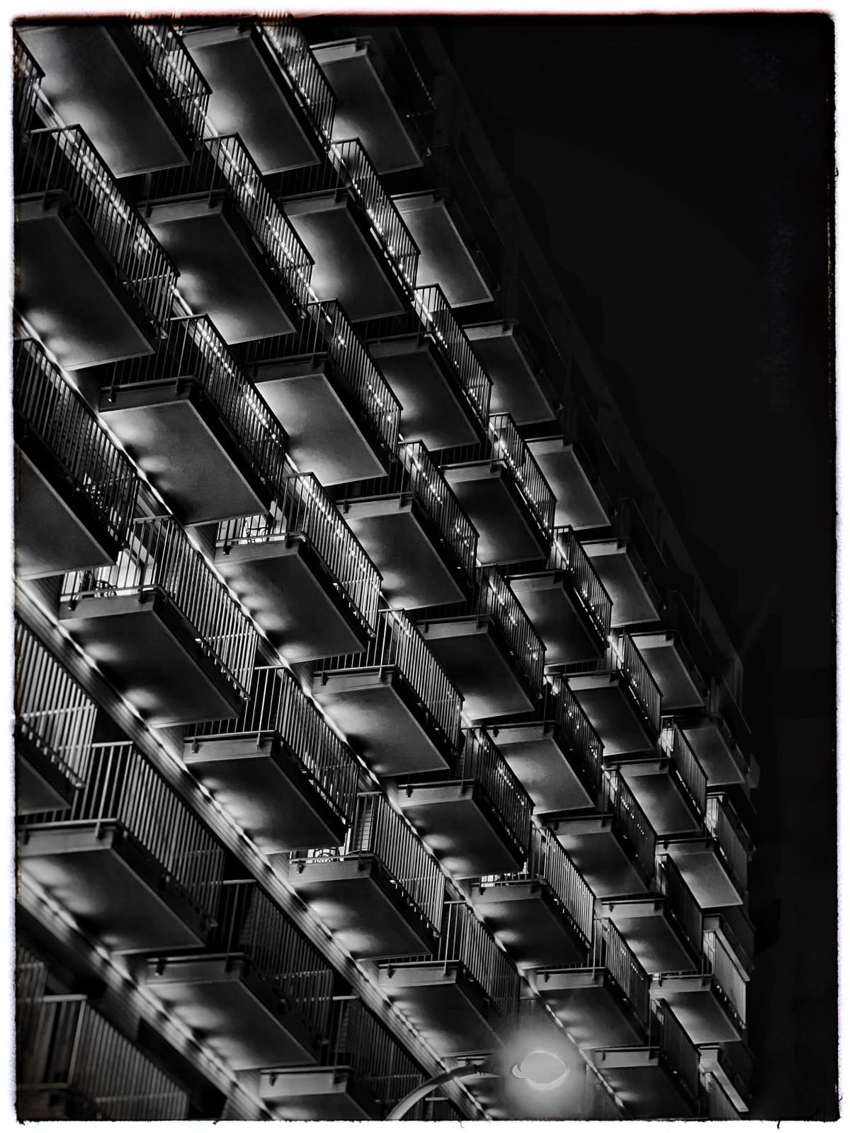 A repeating grid of apartment balconies photographed at night in black and white.