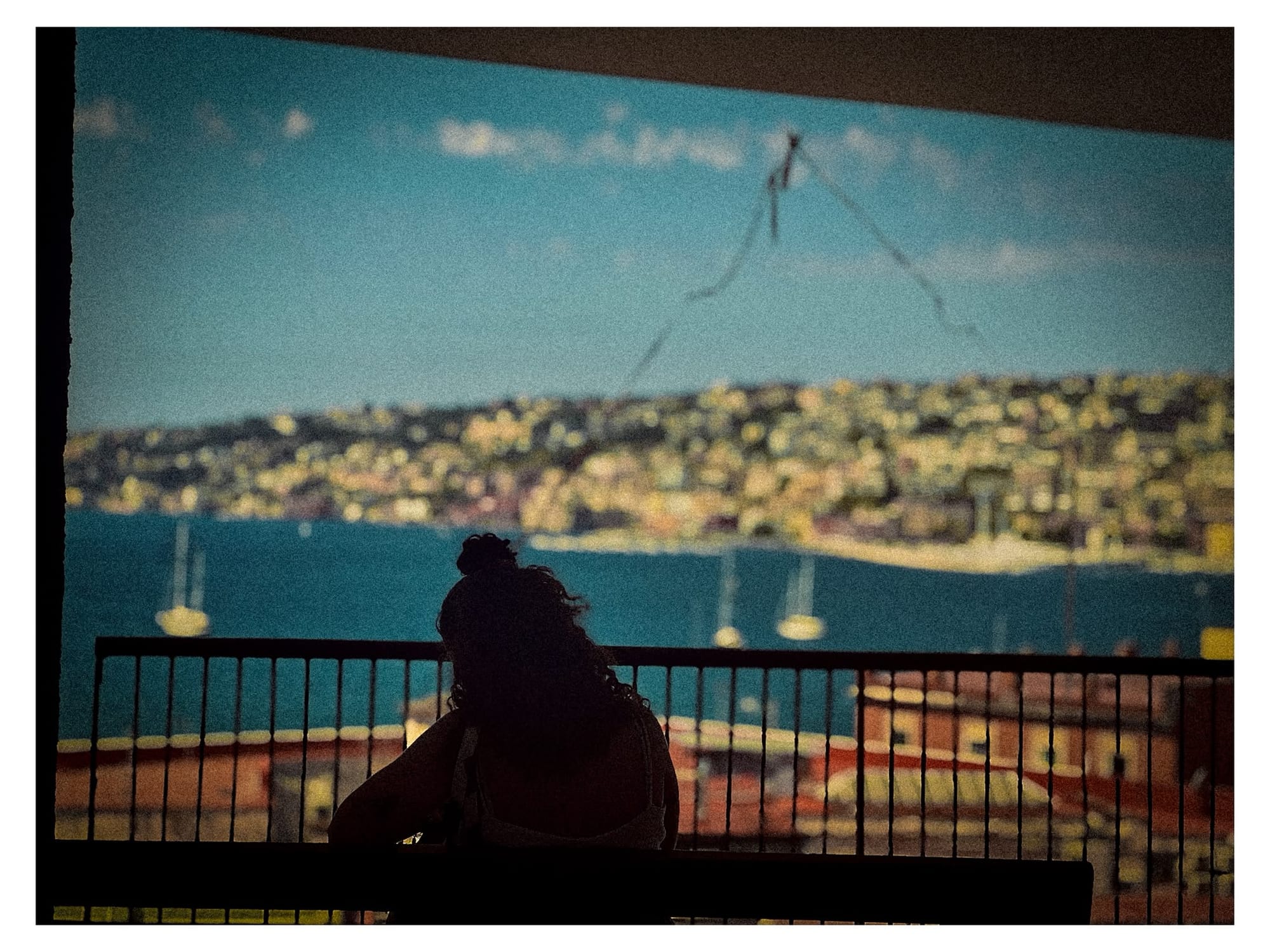 A person silhouetted against a large mural depicting the bay of Naples.