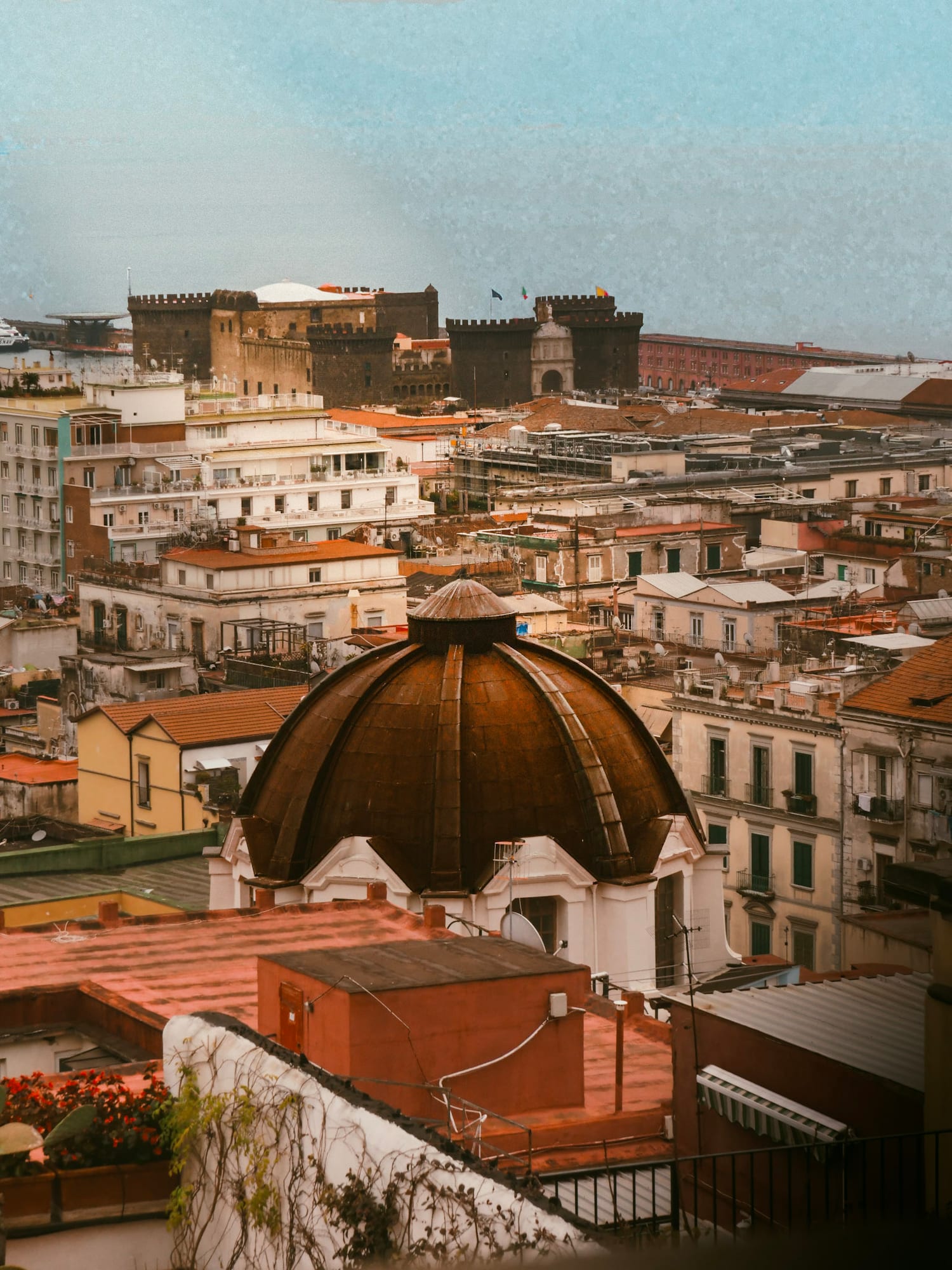 Aerial view of Naples rooftops with the towers of Castel Nuovo and the harbour beyond.