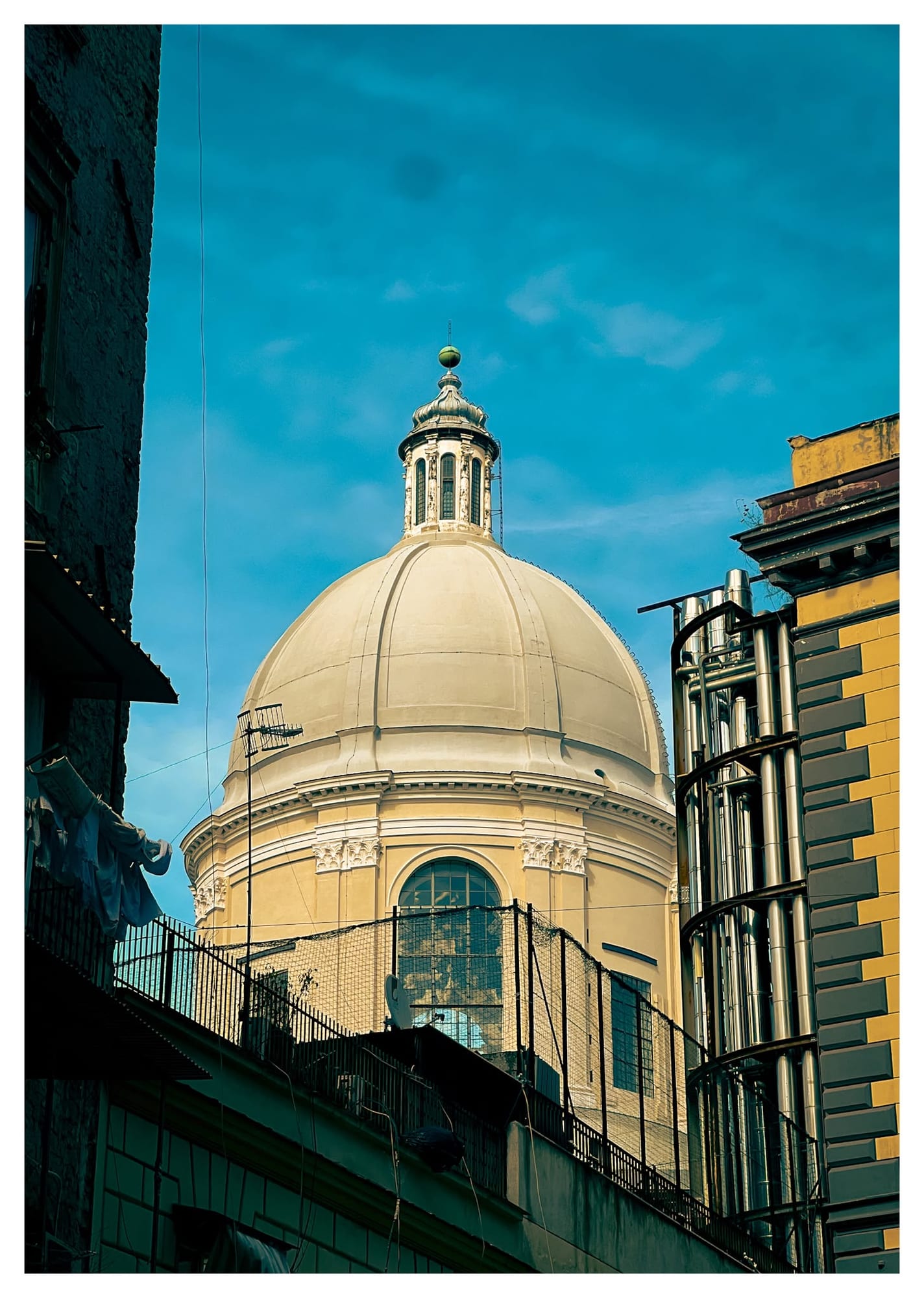 Cream-coloured baroque church dome with a lantern cupola rising above Naples rooftops.