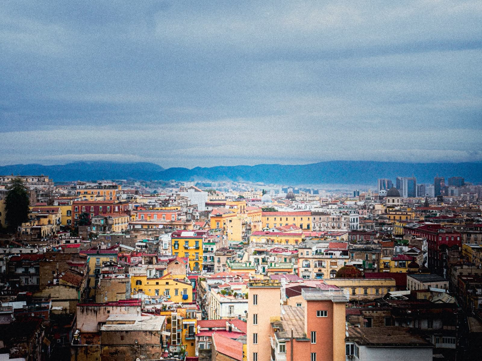 A wide rooftop panorama of central Naples looking toward the skyline and mountains.