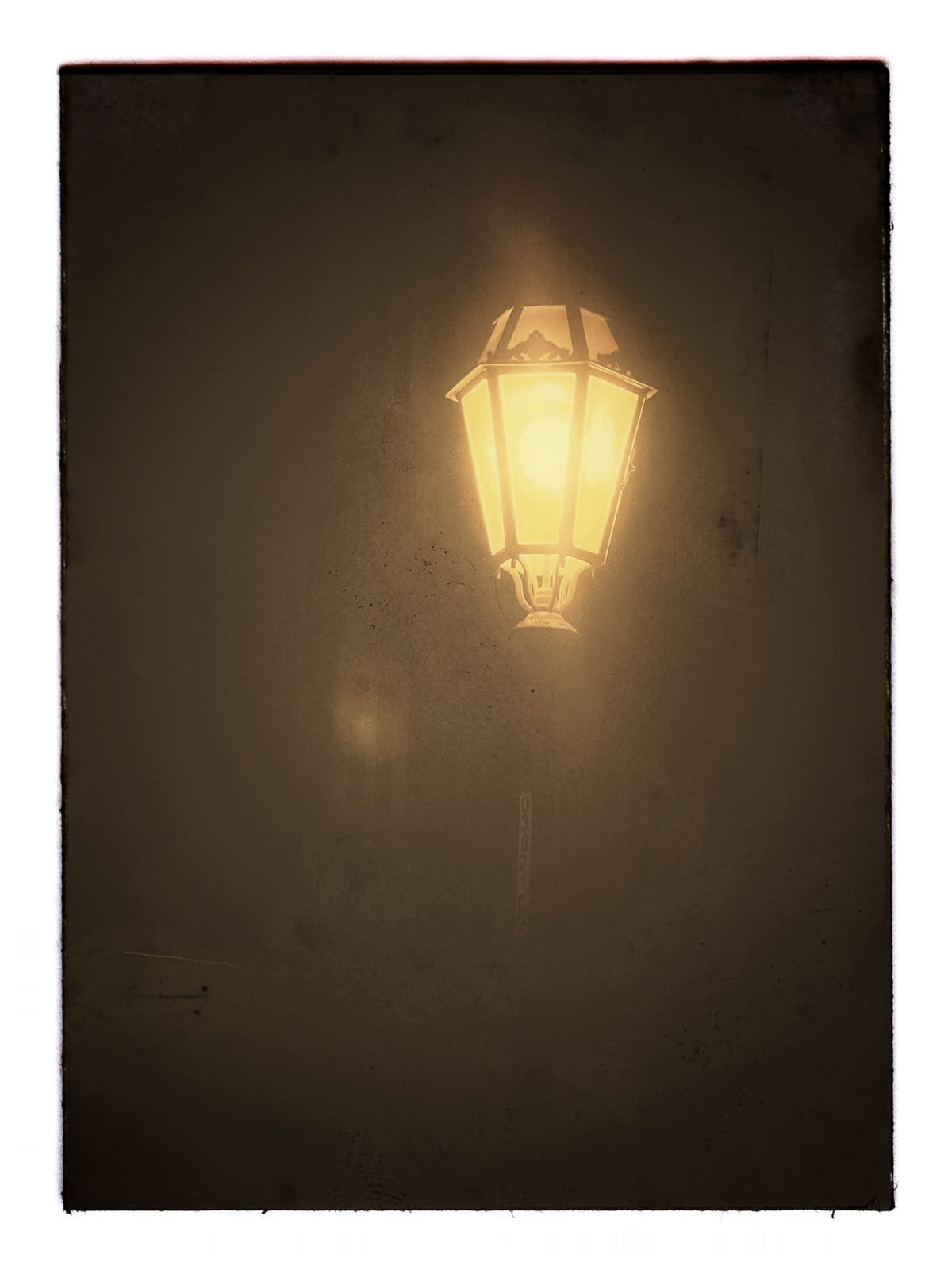 A glowing iron streetlamp isolated against hazy, dark night air.