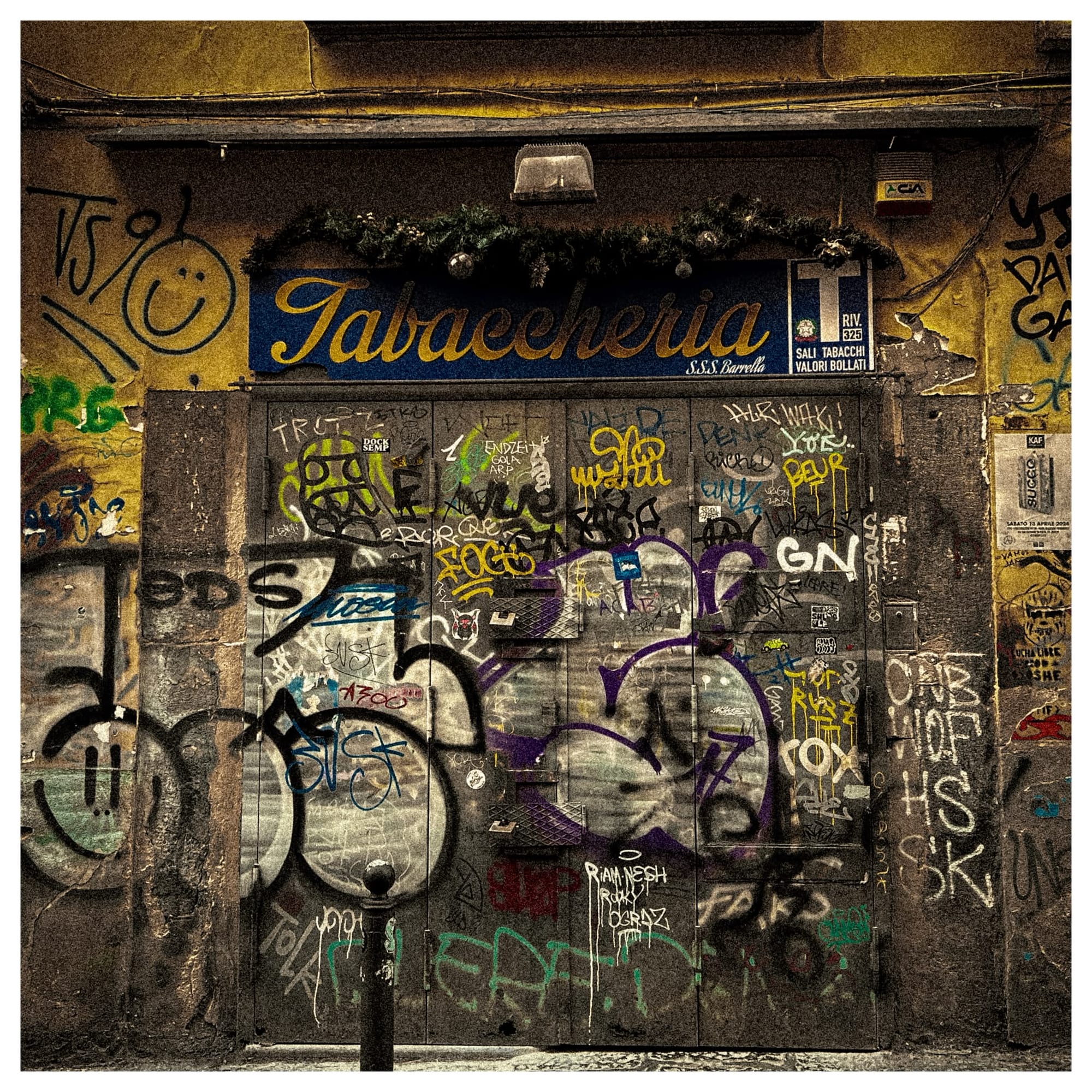A tobacco shop's roll-down shutter completely covered in overlapping graffiti.