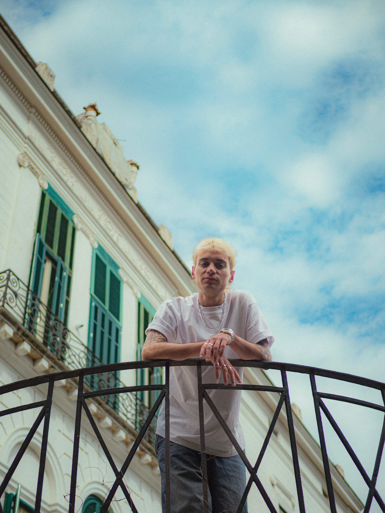 Salar leaning on a wrought-iron balcony rail with a domed church roofline behind him.